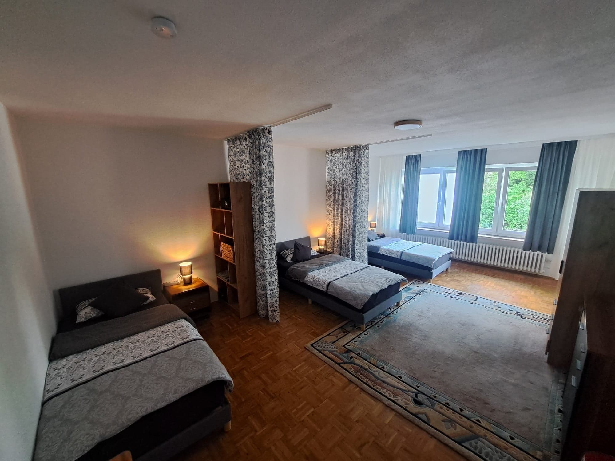 Großer heller Raum der Wohnung C mit drei Einzelbetten, Regal als Raumteiler und Parkettboden
